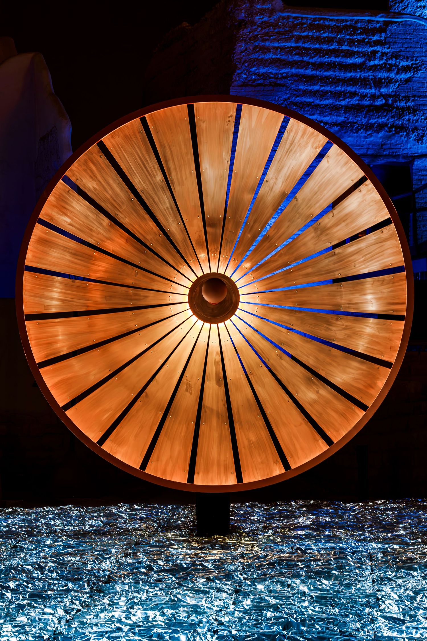 Close-up of illuminated wooden wheel sculpture with symmetrical spokes glowing orange.