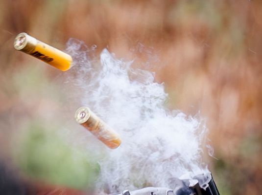 Close-up of shotgun shells ejecting with smoke against autumn background.