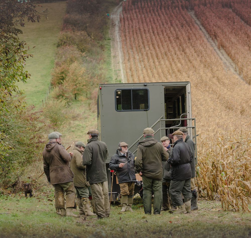 A group of hunters gathered around a mobile hunting blind in an autumn field.