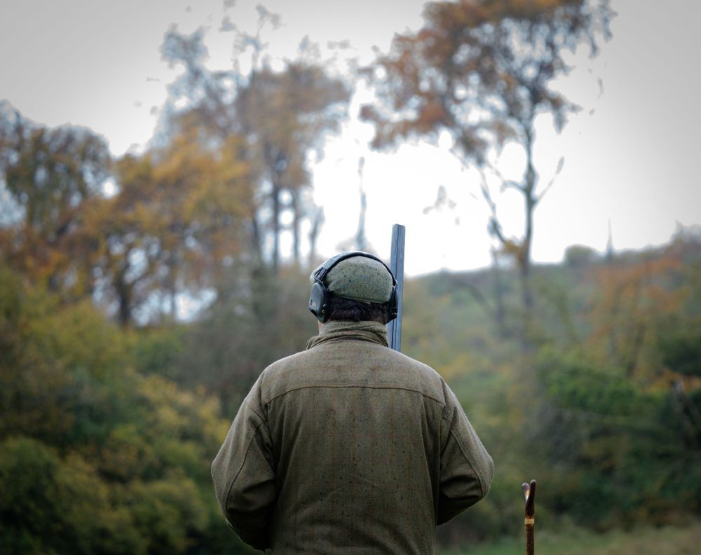 Hunter in olive green attire walking through an autumn field with a rifle during a hunt.