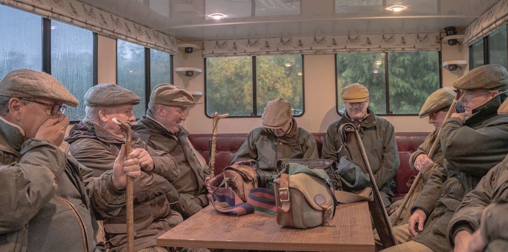 Elderly men in vintage attire sit together in what appears to be a historic train carriage.