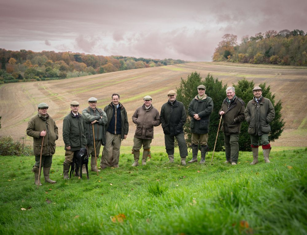 Group of hunters in traditional attire standing on a hillside during an autumn shoot.