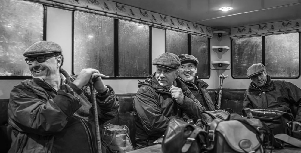 A black and white photo of seniors with walking sticks seated in an old-fashioned railway car.