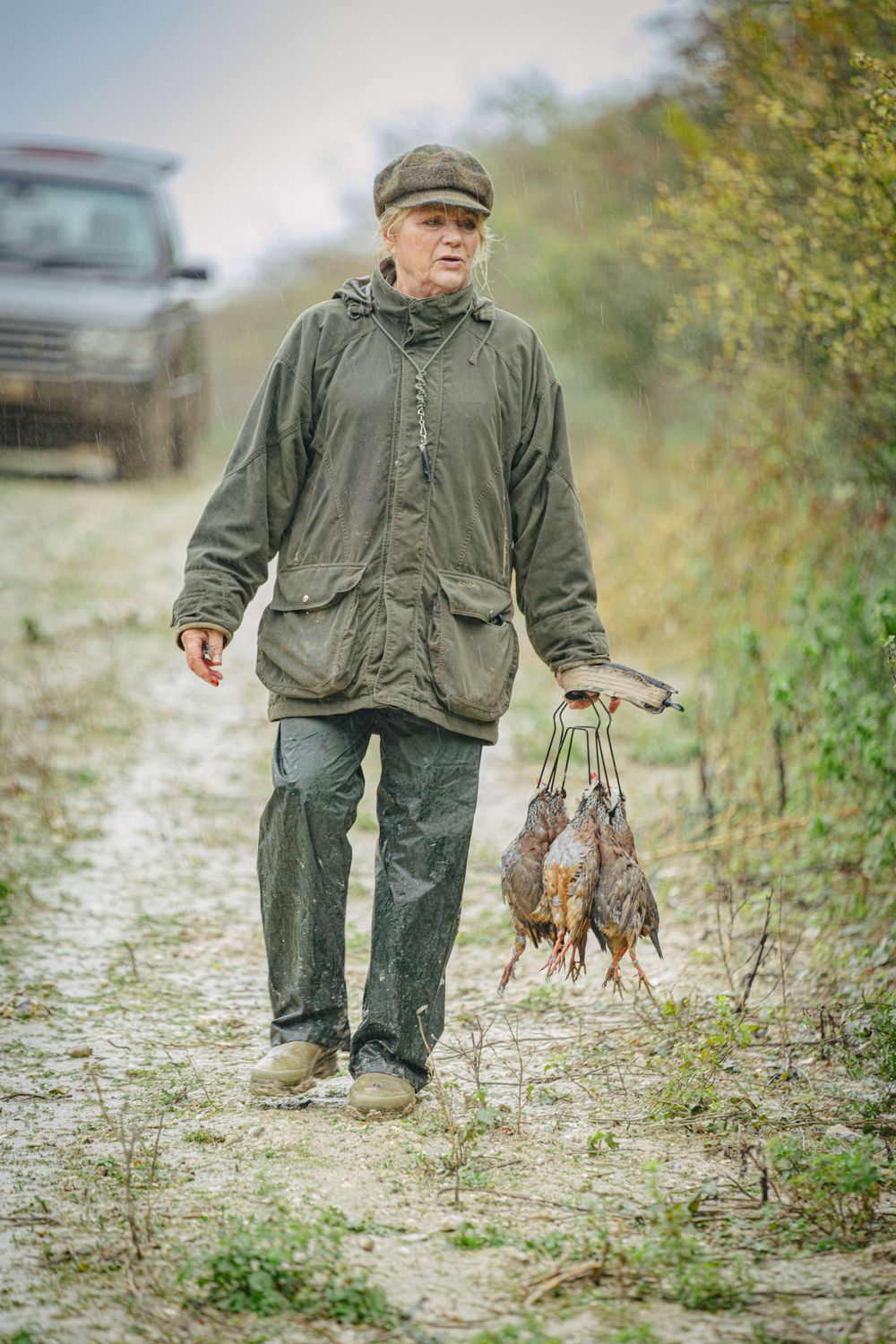 Hunter walking with hunting dogs on a dirt path surrounded by autumn foliage.