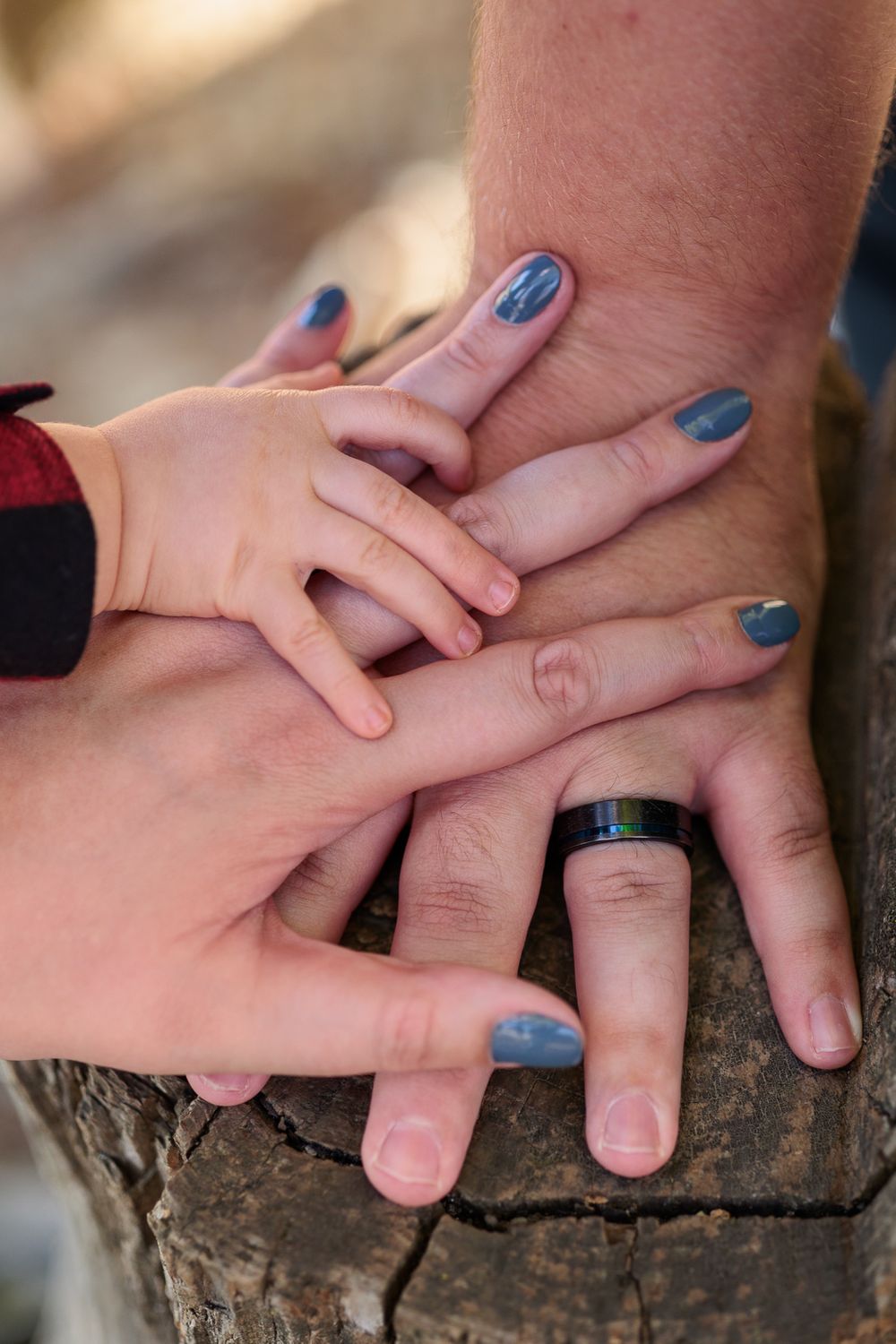 Close-up of mom, dad and babies hands resting together on a wooden surface.
