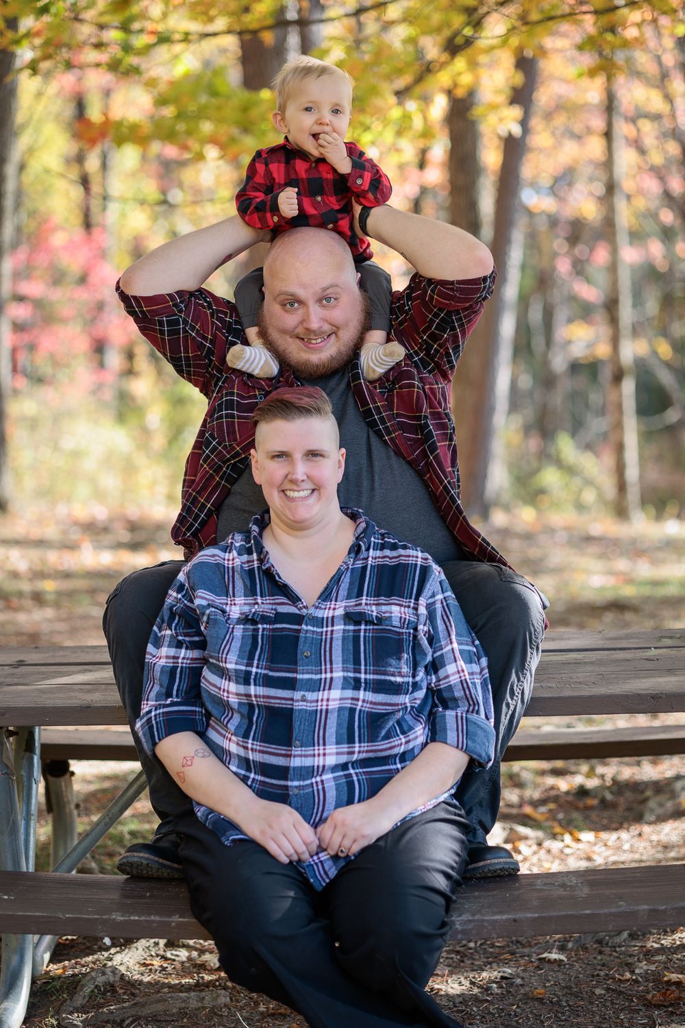 Family members in coordinating plaid shirts sitting stacked on wooden bench outdoors.