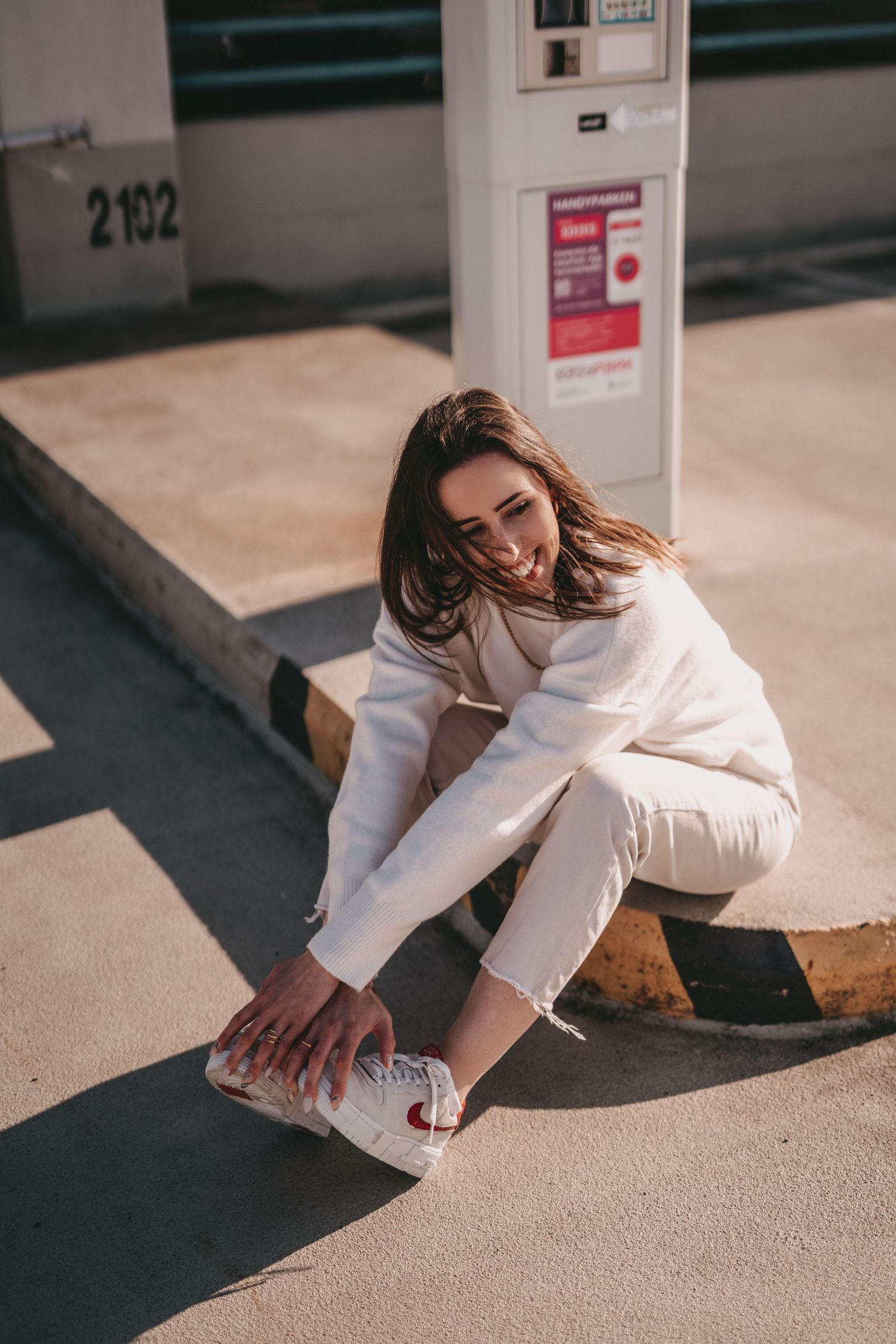 Playful portrait adjusting shoe while sitting on concrete ledge in parking structure.