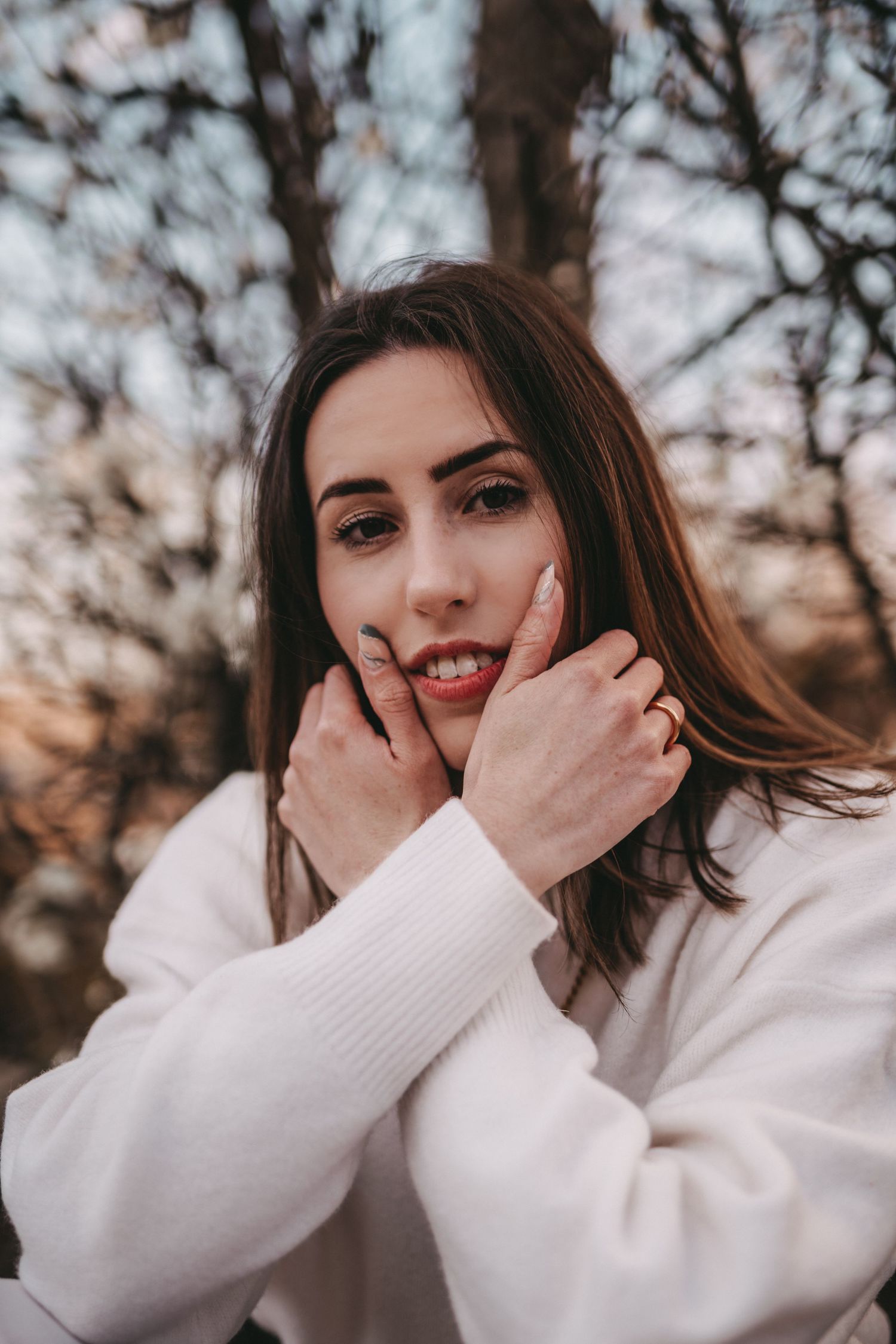 A person in a white sweater poses outdoors against a blurred autumn background.