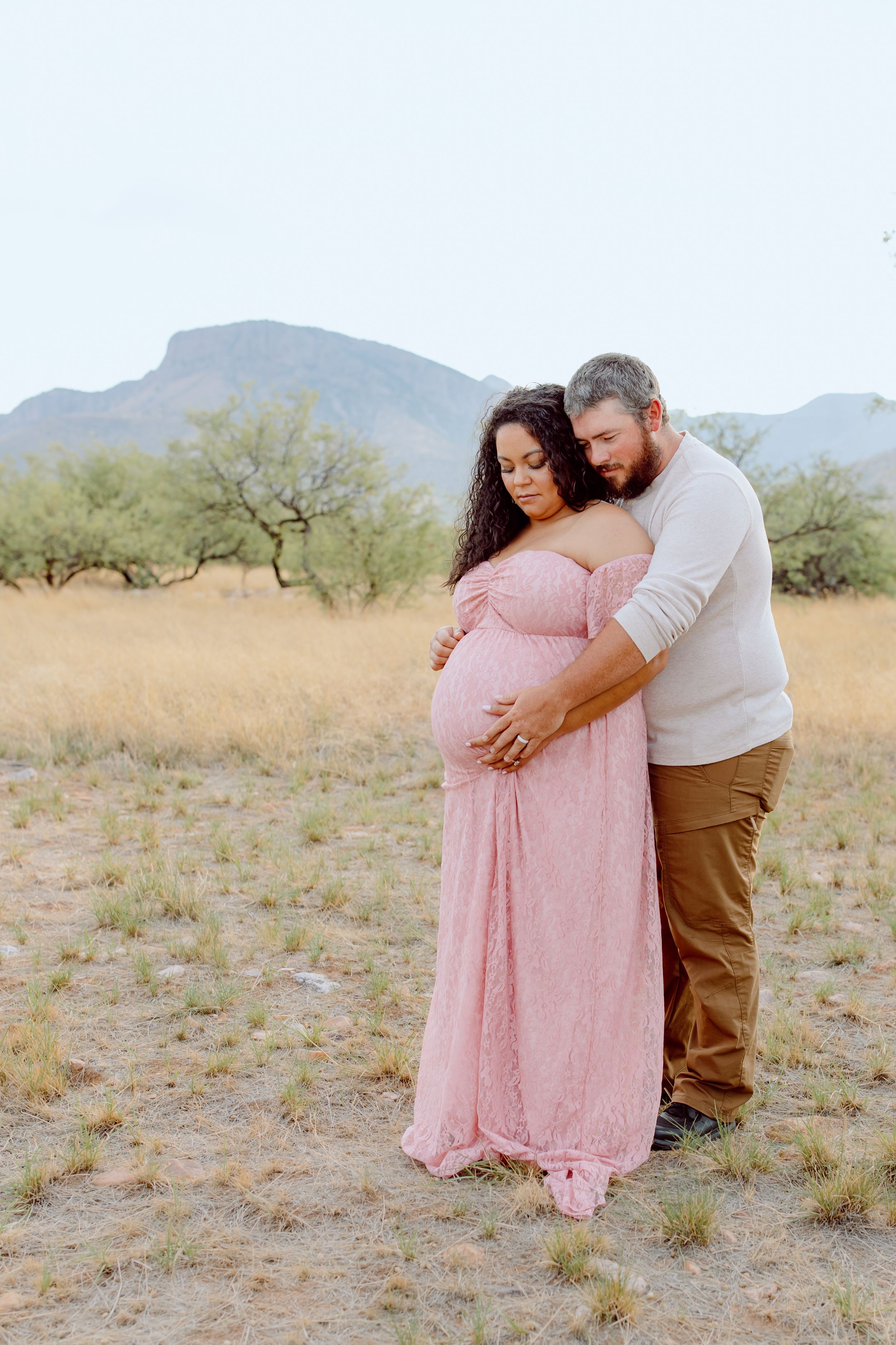 Tender maternity moment captured in desert setting with mountains behind.