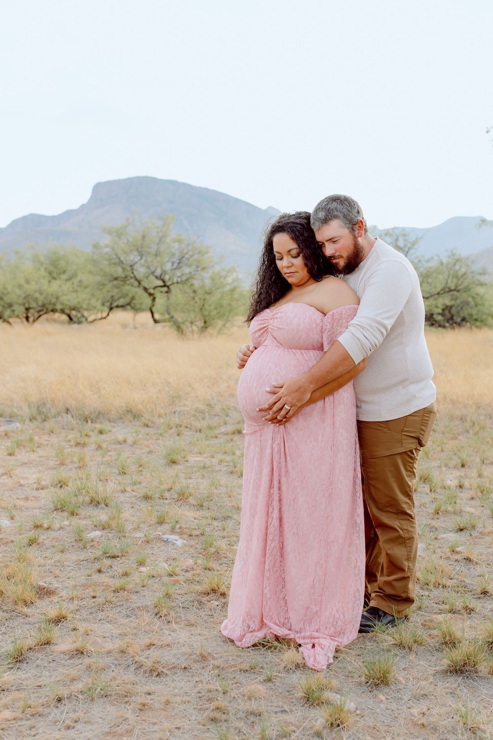 Tender maternity moment captured in desert setting with mountains behind.
