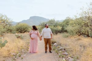 Two people stroll together on a desert path surrounded by desert vegetation and mountains.