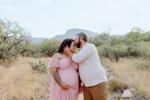 A couple shares an intimate moment in the desert with mountains and cacti in the background.