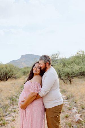 A romantic desert photoshoot featuring a couple in pink and white against mountain scenery.