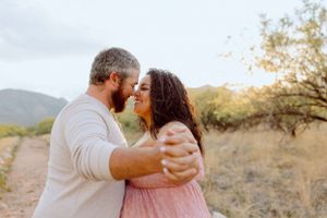 A romantic couple embraces on a desert trail during golden hour with mountains in the background.