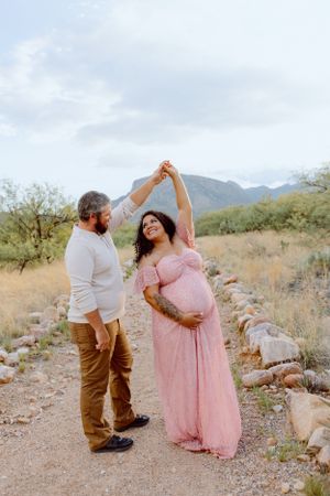 A couple dances on a desert trail during a maternity photoshoot.