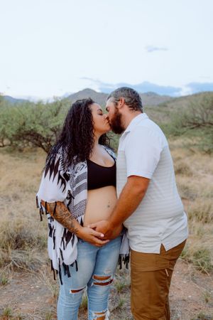 A couple poses for a maternity photo in casual wear against a desert backdrop.