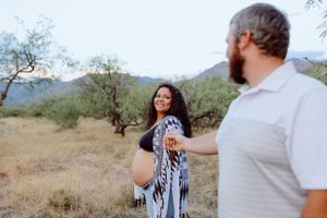 Couple embraces in a desert landscape with mountains and desert brush in the background.