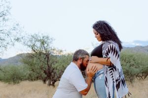 A tender maternity moment captured in a desert setting with mountains in the background.