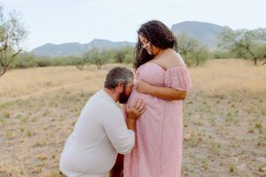 Intimate desert maternity photos with couple in pink dress and casual attire.