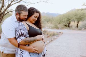 Couple embracing outdoors with desert mountains and saguaro cacti in the background.