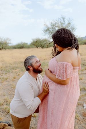 Sweet maternity moment in pink lace dress against desert backdrop.