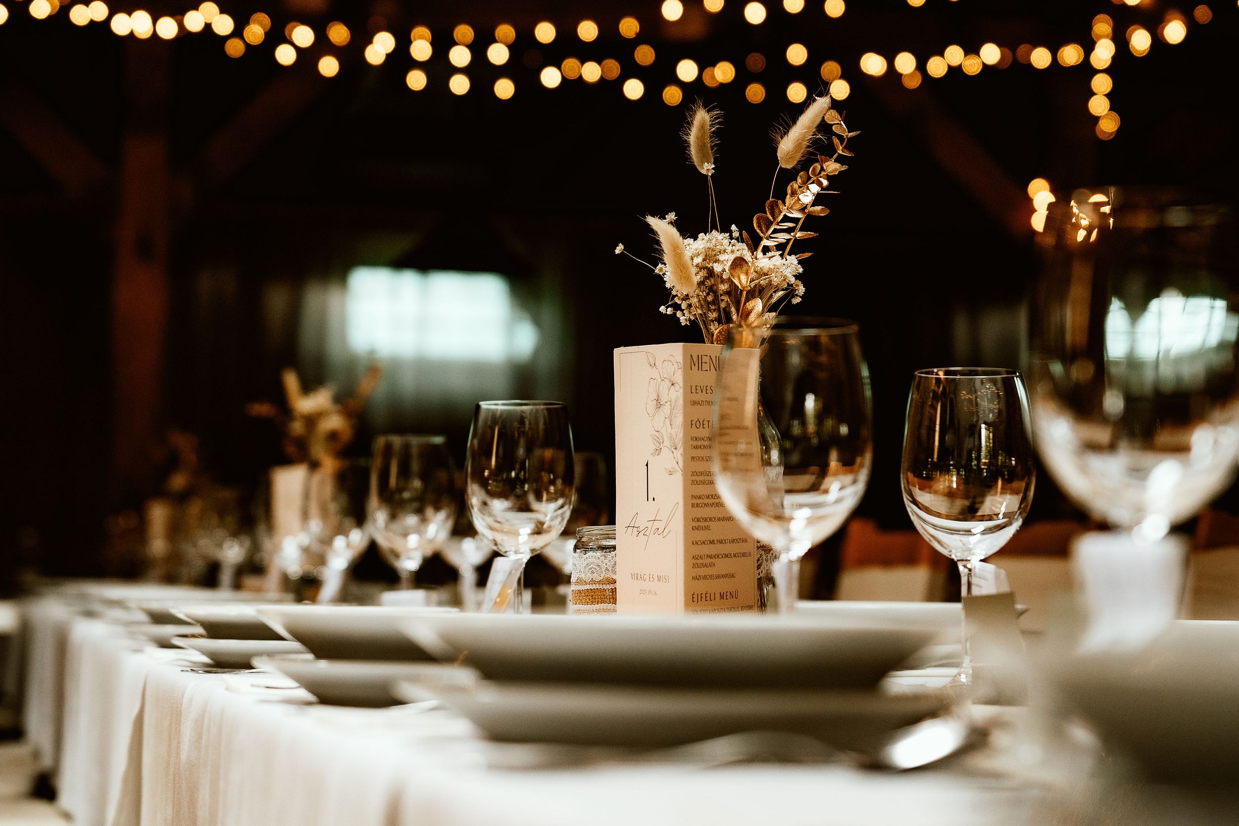 Elegant wedding table setting with white linens, wine glasses and string lights creating a romantic ambiance.