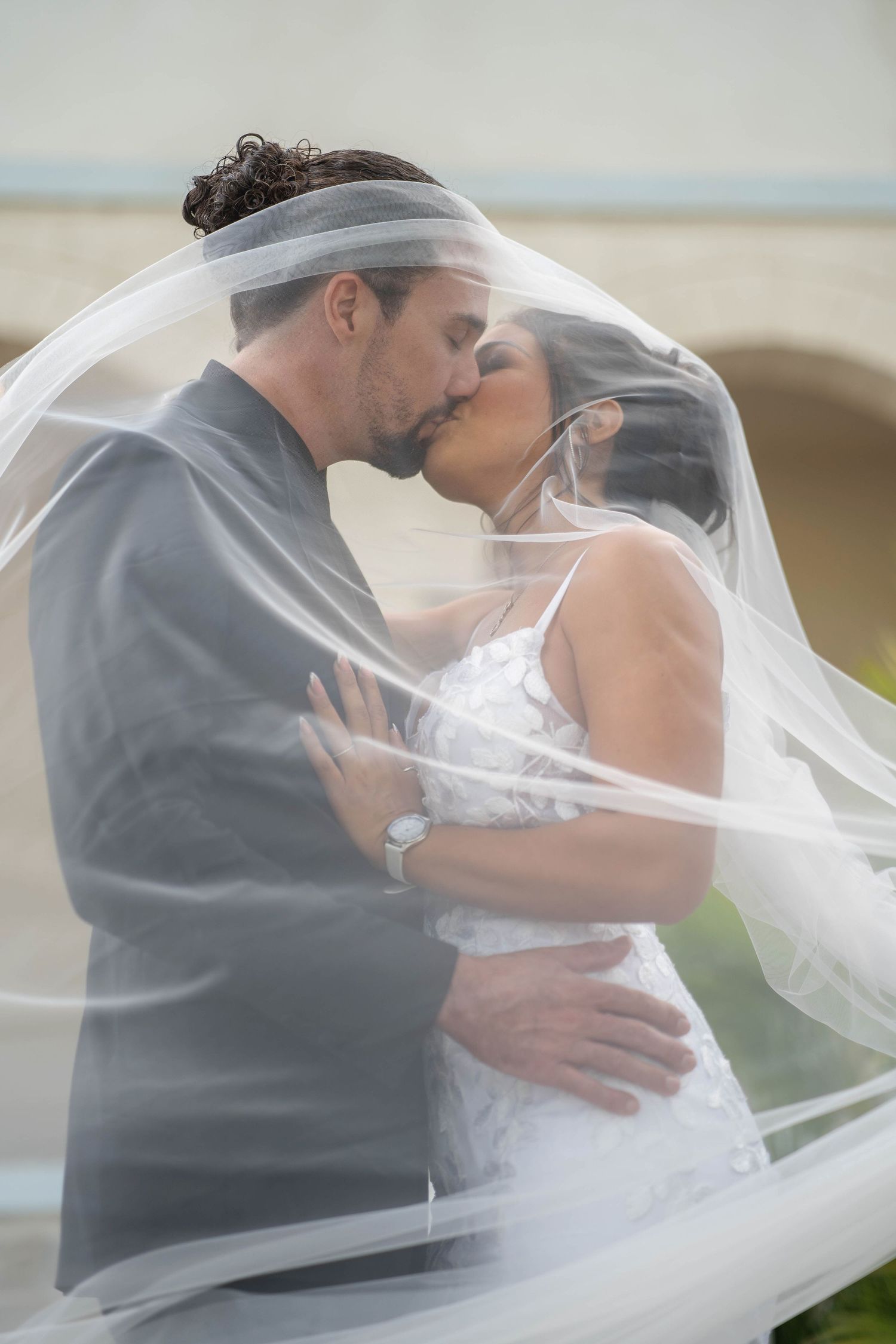 Bride and groom share a romantic kiss under flowing white veil on their wedding day.