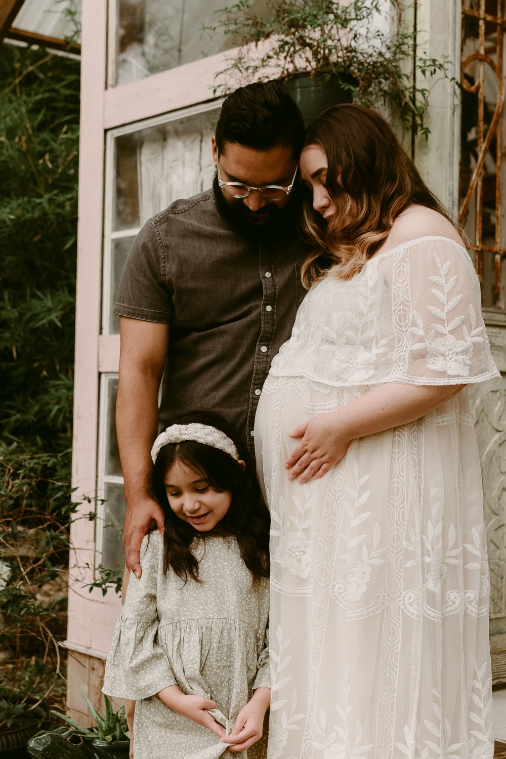A family poses together against a pink door in white outfits.