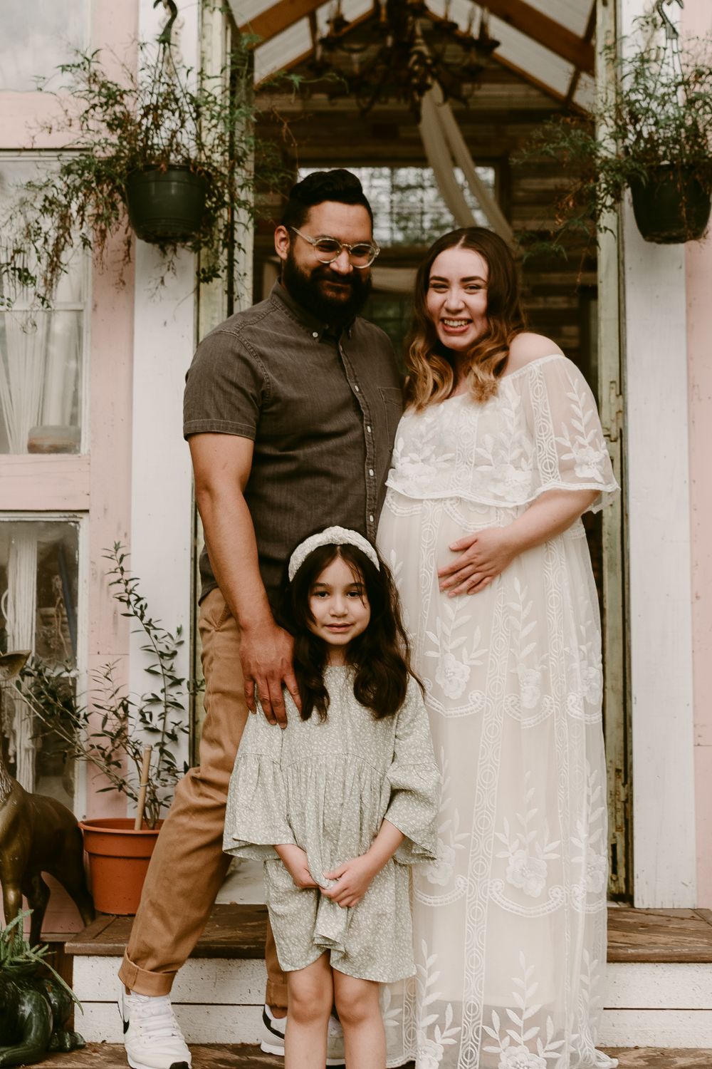 A family of three poses for a maternity portrait on their front porch steps.