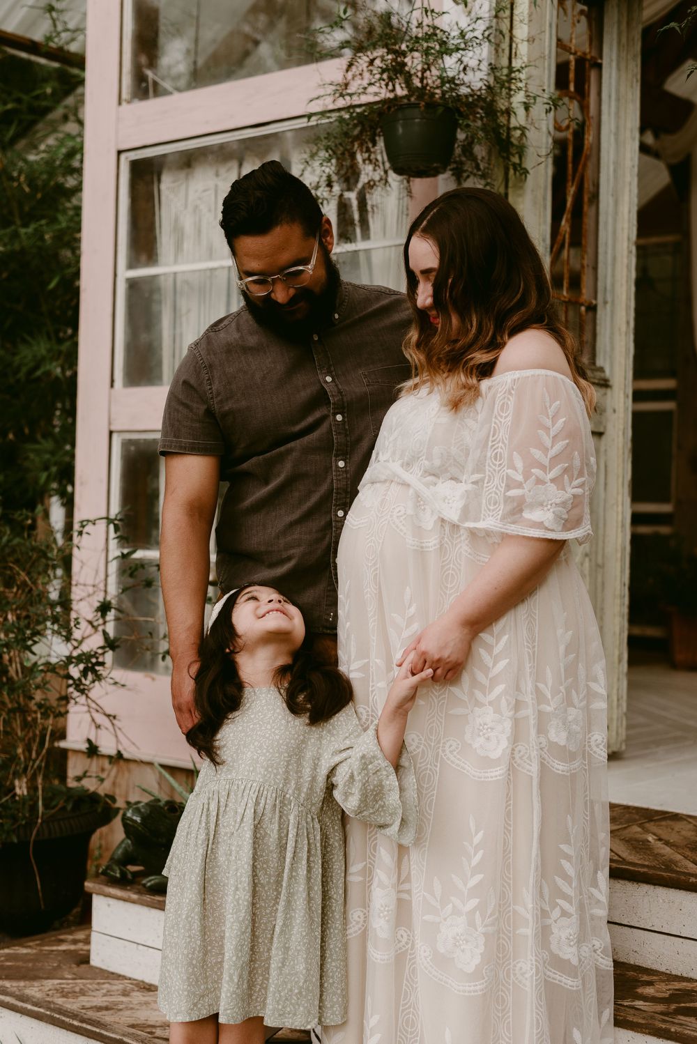 A joyful family moment captured during a maternity photoshoot on their front porch.