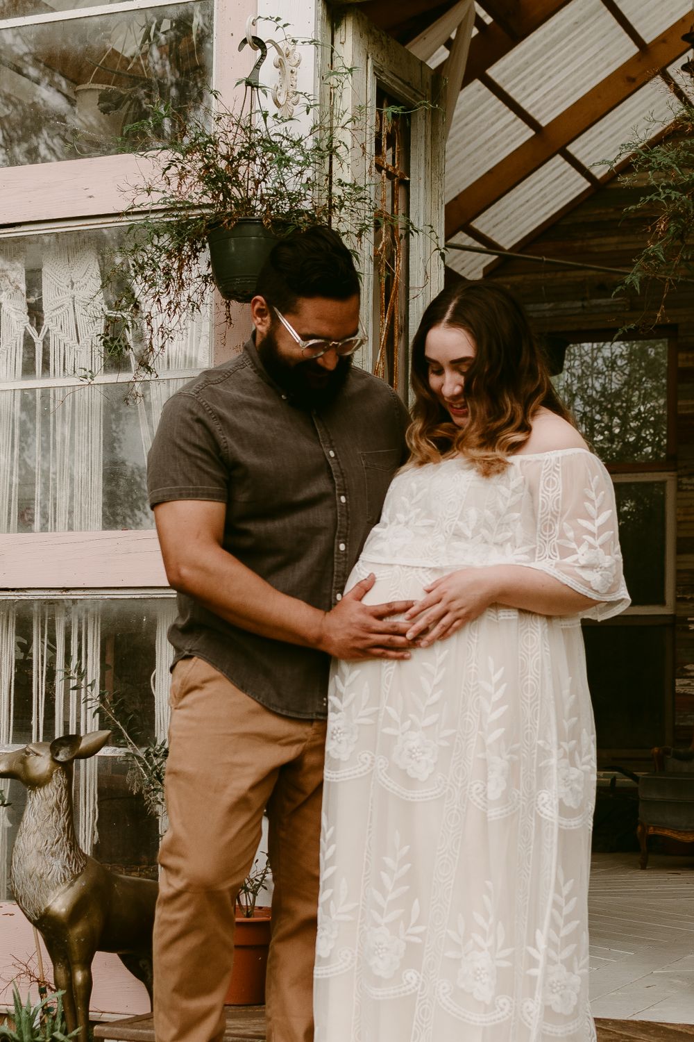 An intimate maternity photo shows a couple embracing on their rustic porch.
