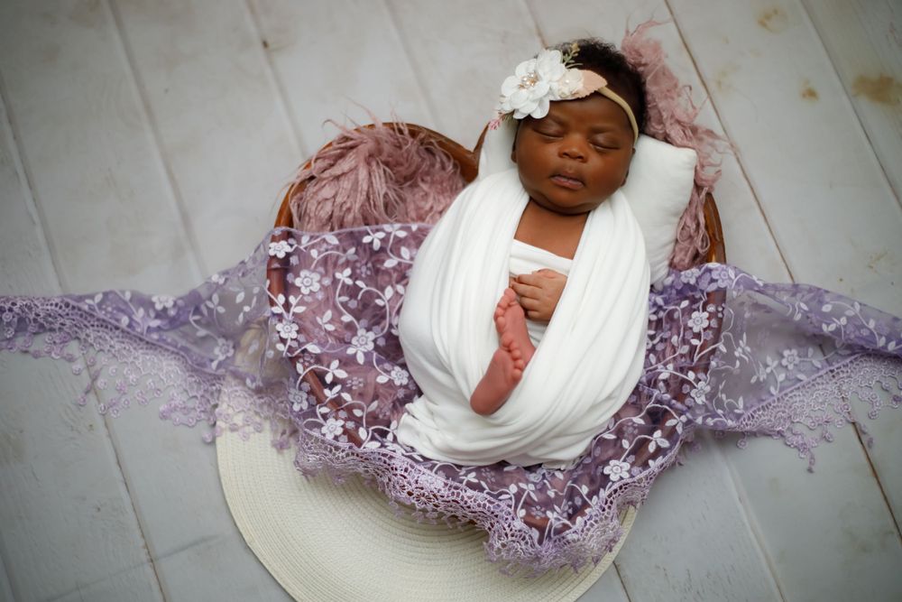 Sleeping newborn on purple sequin fabric with white wrap and floral accessory.