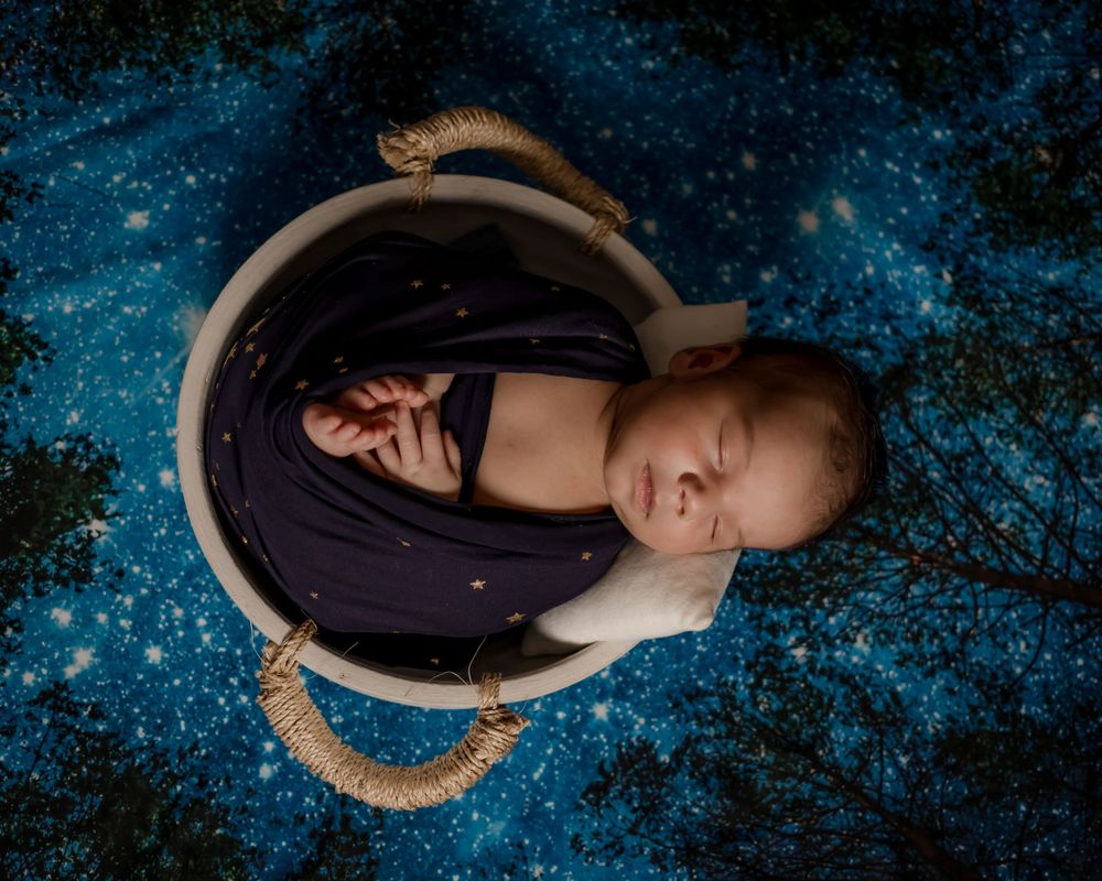 Sleeping newborn in nautical themed basket against starry night background.