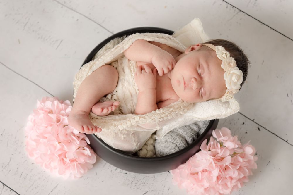 Sleeping newborn in black basket with pink flowers and white blanket.