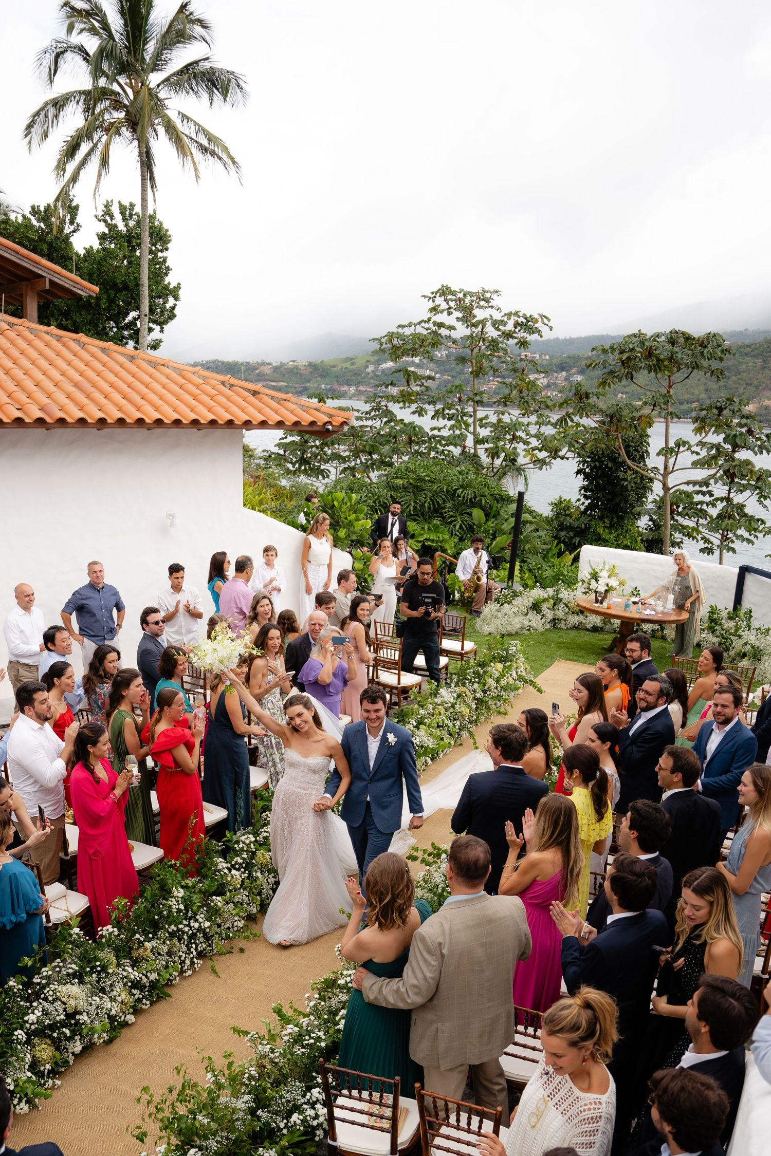 Aerial view of outdoor wedding ceremony with palm trees and mountain vista in background.