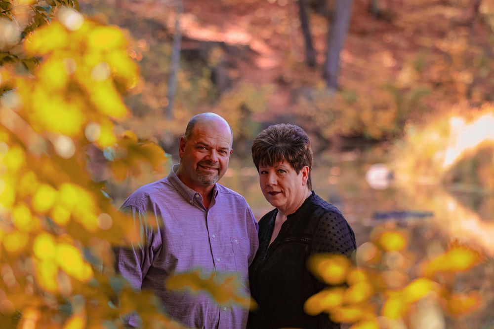 Couple embracing outdoors with golden autumn leaves in background during sunset.