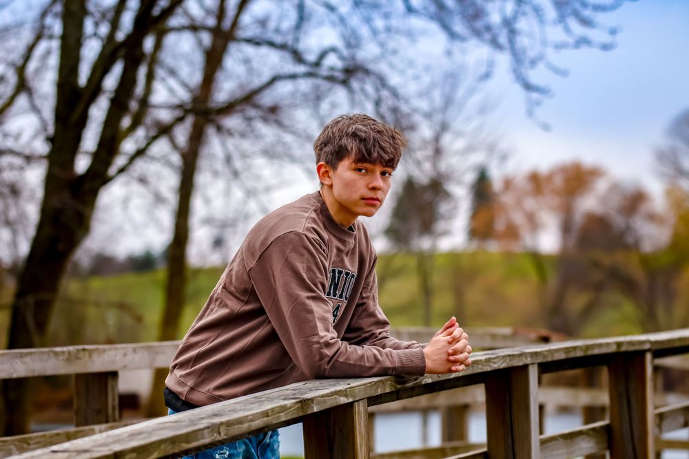 Outdoor portrait on wooden bridge with autumn trees in background.