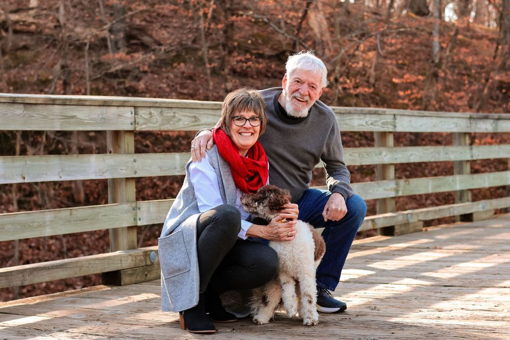 Two people sit with their dog on wooden bridge during autumn season.