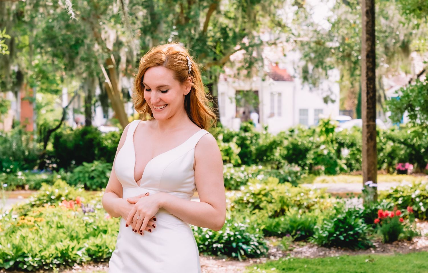 A bride smiles big while looking down at her hand with her wedding ring held out.