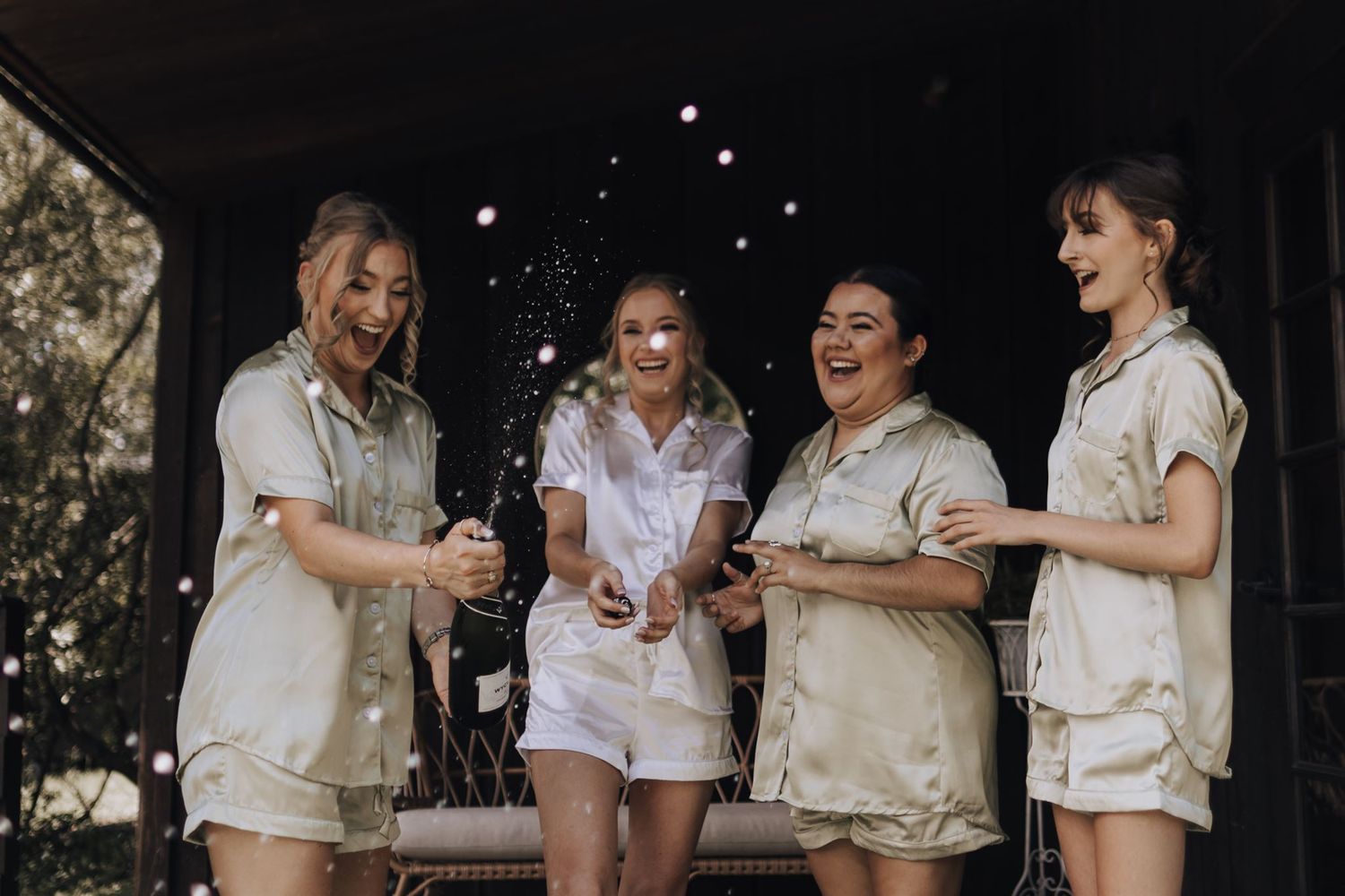 Friends in matching cream colored loungewear share drinks and laughter.