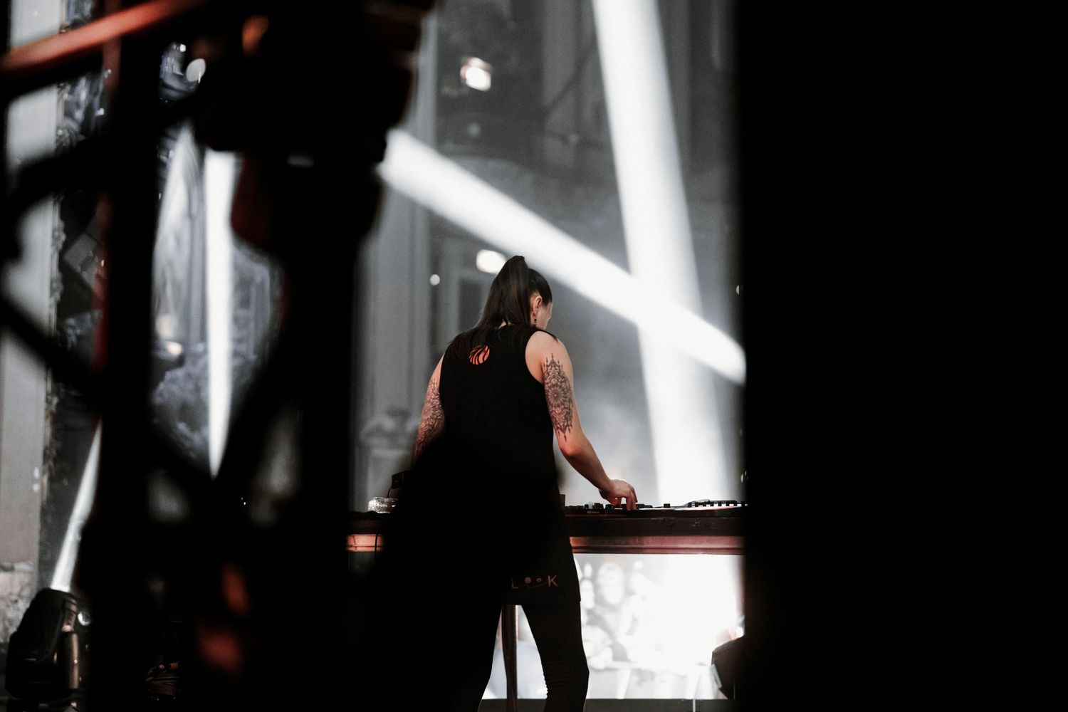 DJ performing in dramatic side lighting with bright white spotlight beams cutting through darkness.
