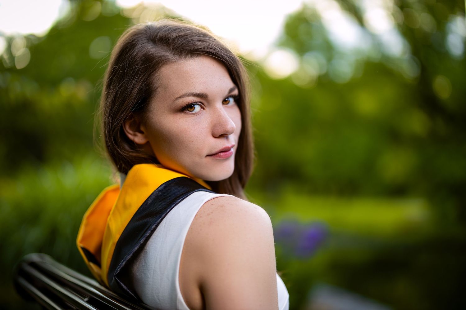Graduation portrait in an outdoor garden setting with yellow accent and blurred natural background.