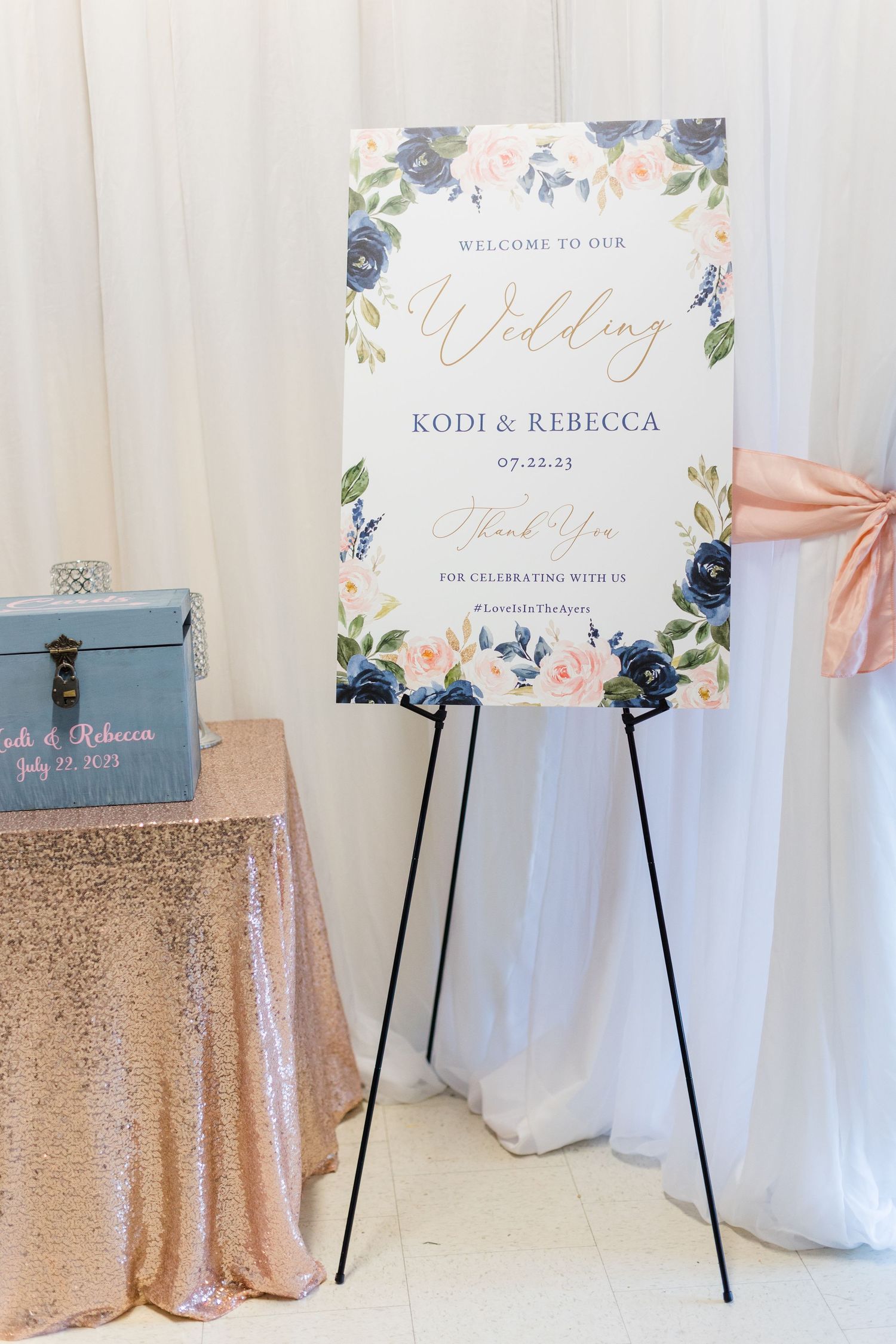 Floral wedding welcome sign on easel with rose gold sequin tablecloth.