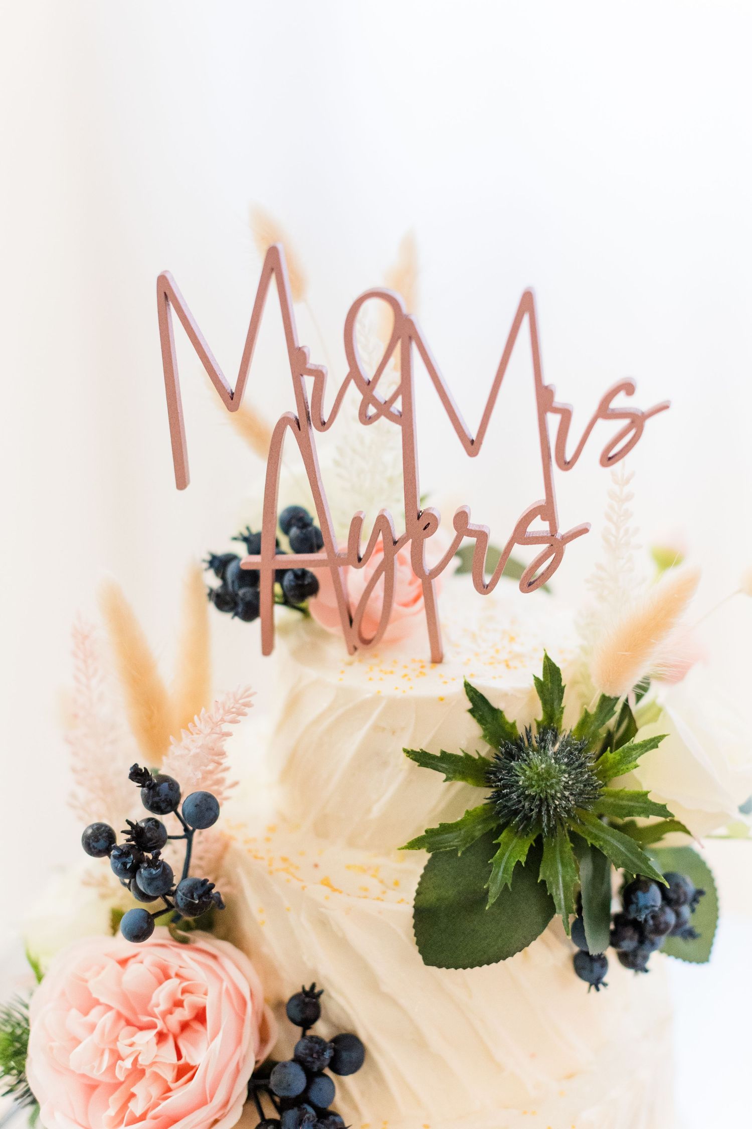 Rose gold Mr & Mrs cake topper with floral accents on white wedding cake.