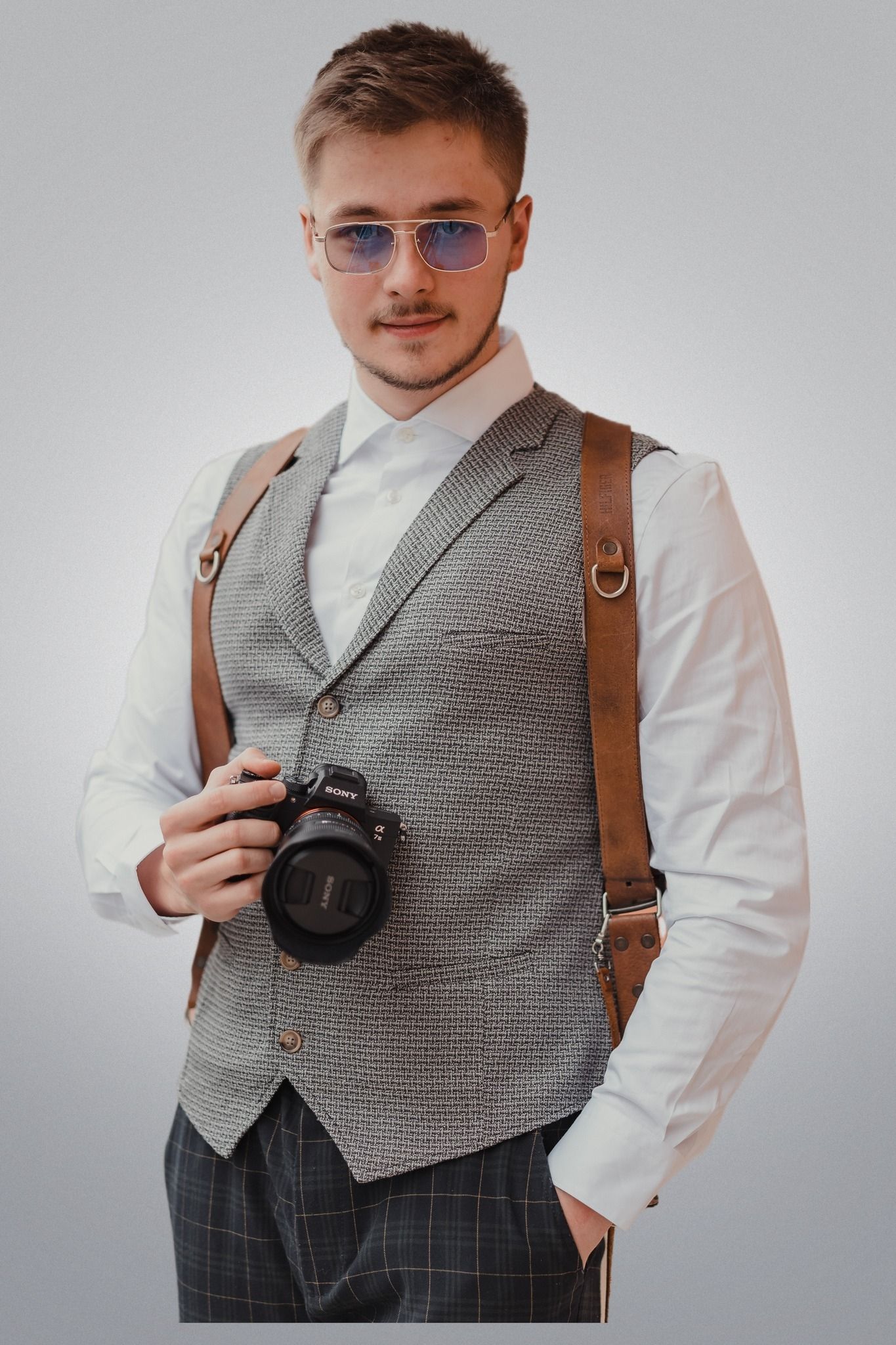 Professional photographer wearing a gray vest and white shirt adjusts camera equipment in studio.