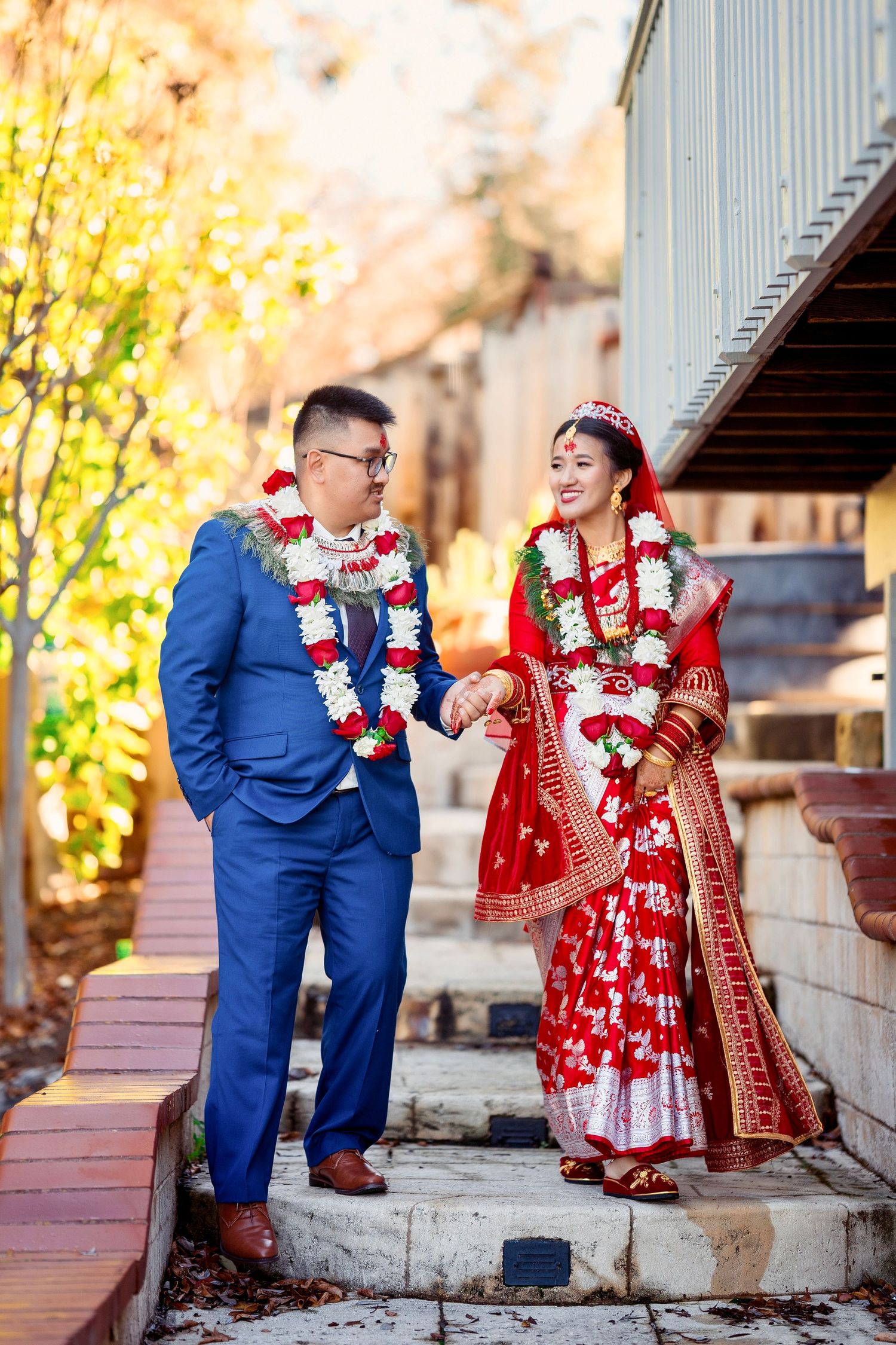 A couple in wedding attire sharing a moment on outdoor steps with autumn foliage.