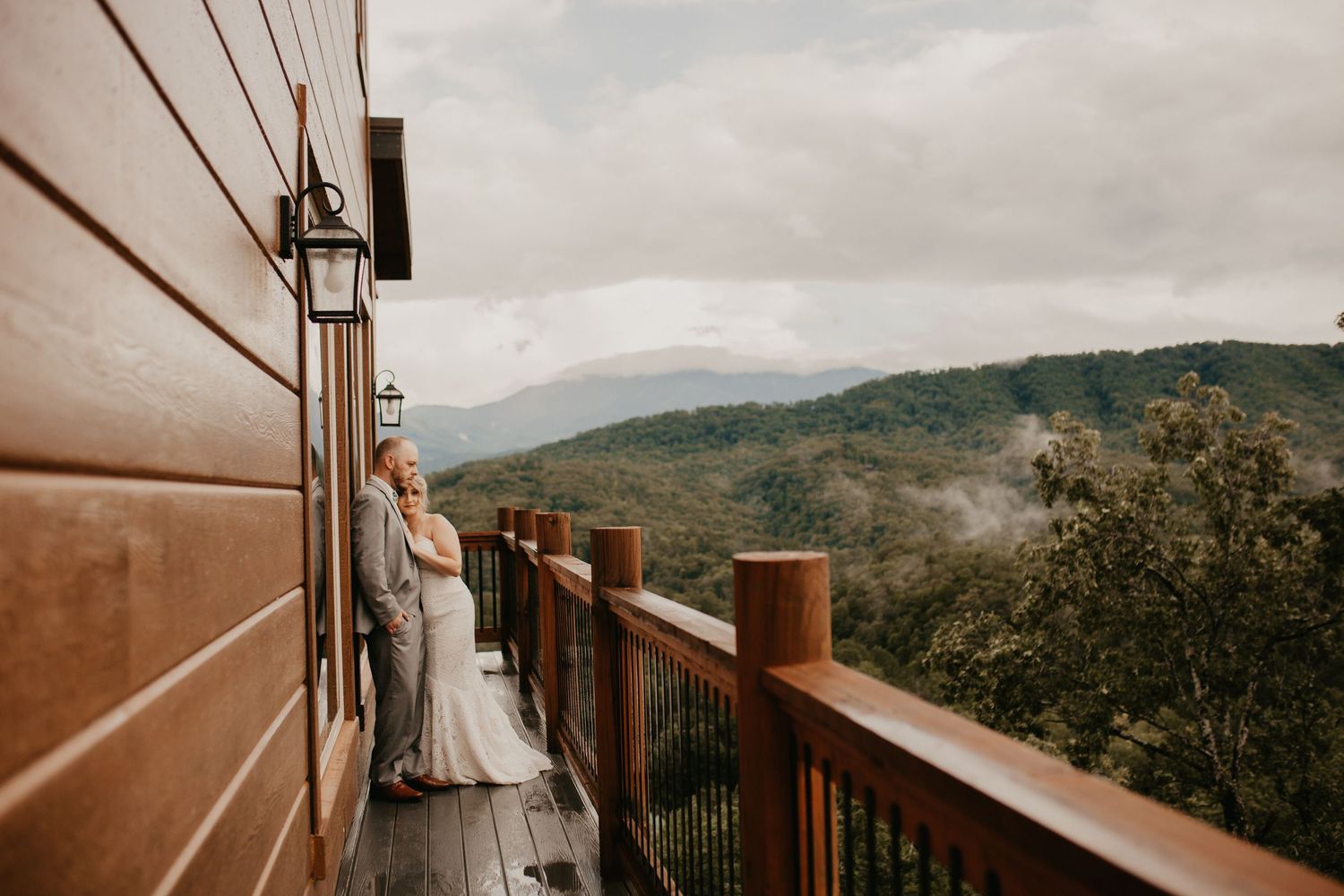 A rustic wooden deck overlooking a scenic mountain landscape with green rolling hills and distant trees in the background.