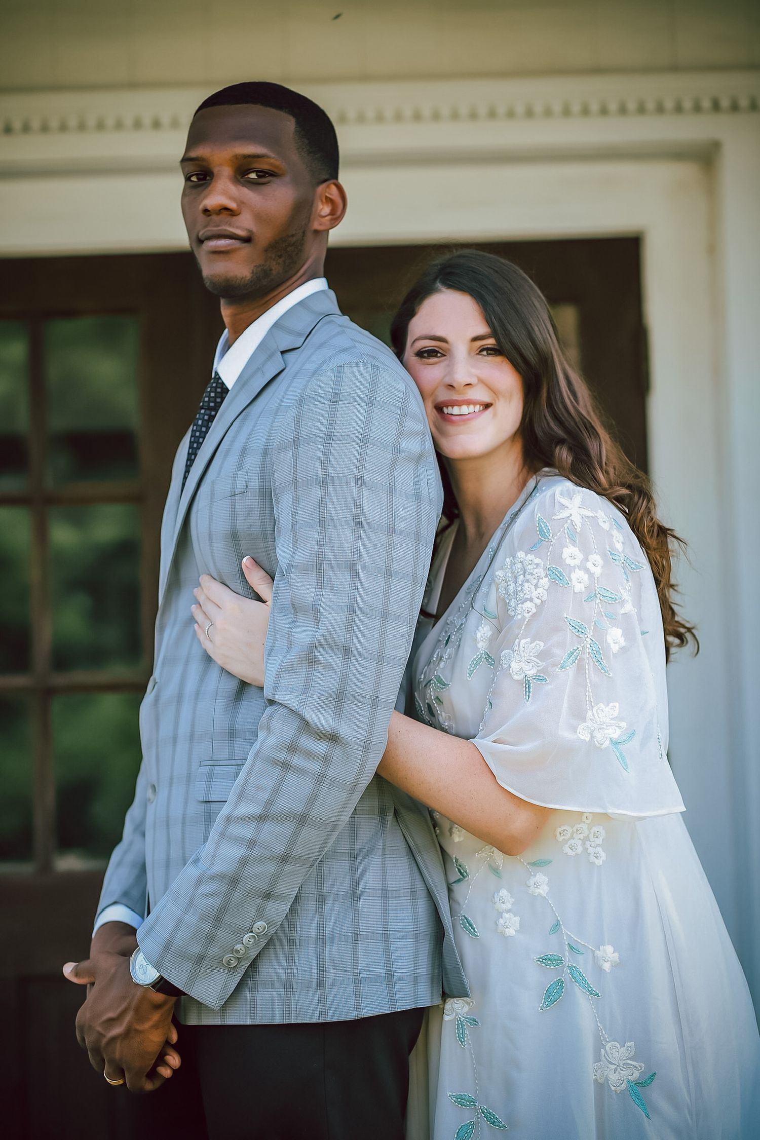 Couple in elegant spring attire poses together outside classic white building.
