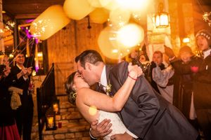 Romantic first dance moment under glowing lights and balloons at rustic wedding reception.