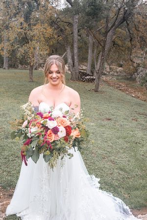 Bride in white gown holds colorful autumn bouquet in outdoor garden setting.